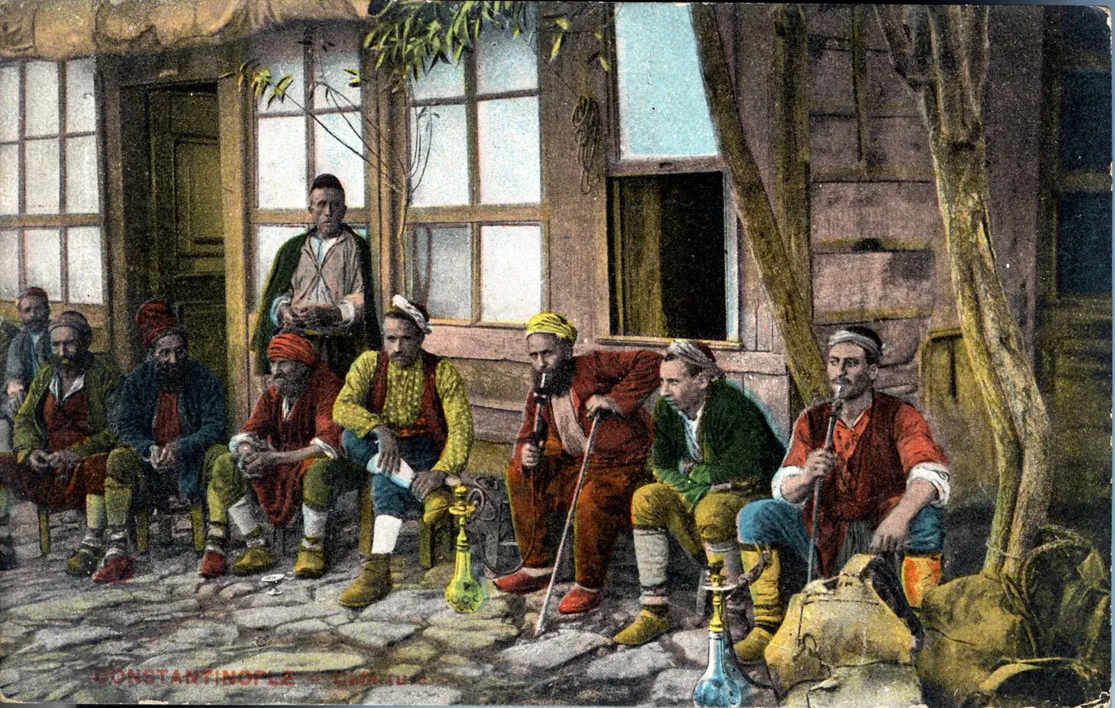 Carte postale photographique montrant un groupe d'hommes coiffés du fez assis sur des tabourets devant la façade d'un café ottoman, tasses et narguiles posés devant eux.
