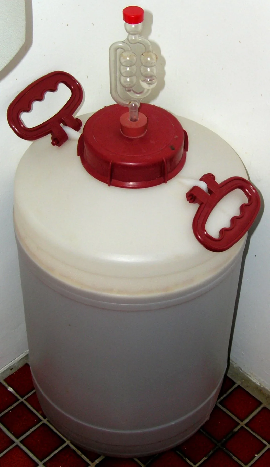 Une cuve de fermentation en plastique alimentaire, fermée par un couvercle et surmontée d'un barboteur à bulles rempli d'eau