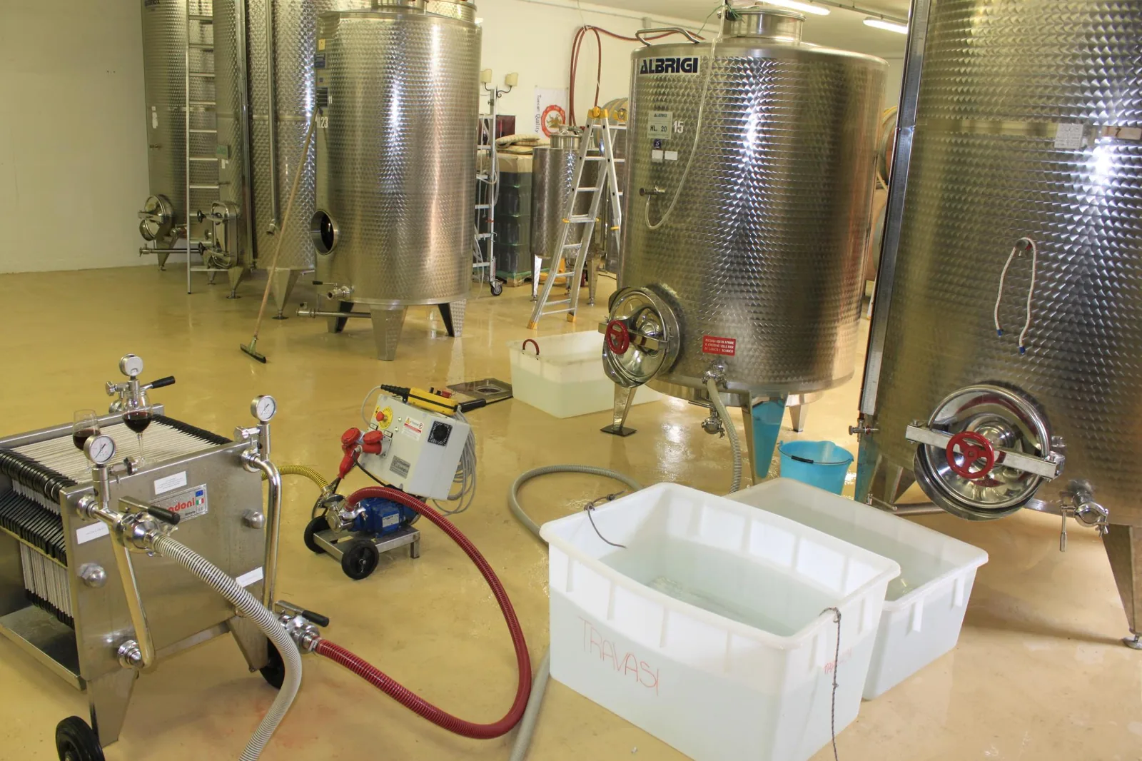 Plusieurs cuves de fermentation fermées en inox, munies de vannes à volant rouge et de manomètres, alignées dans le local d'une cave à vin ; l'image montre du matériel de vinification, mais les cuves fermées à vannes et manomètres sont du même type que celles utilisées pour la fermentation du café