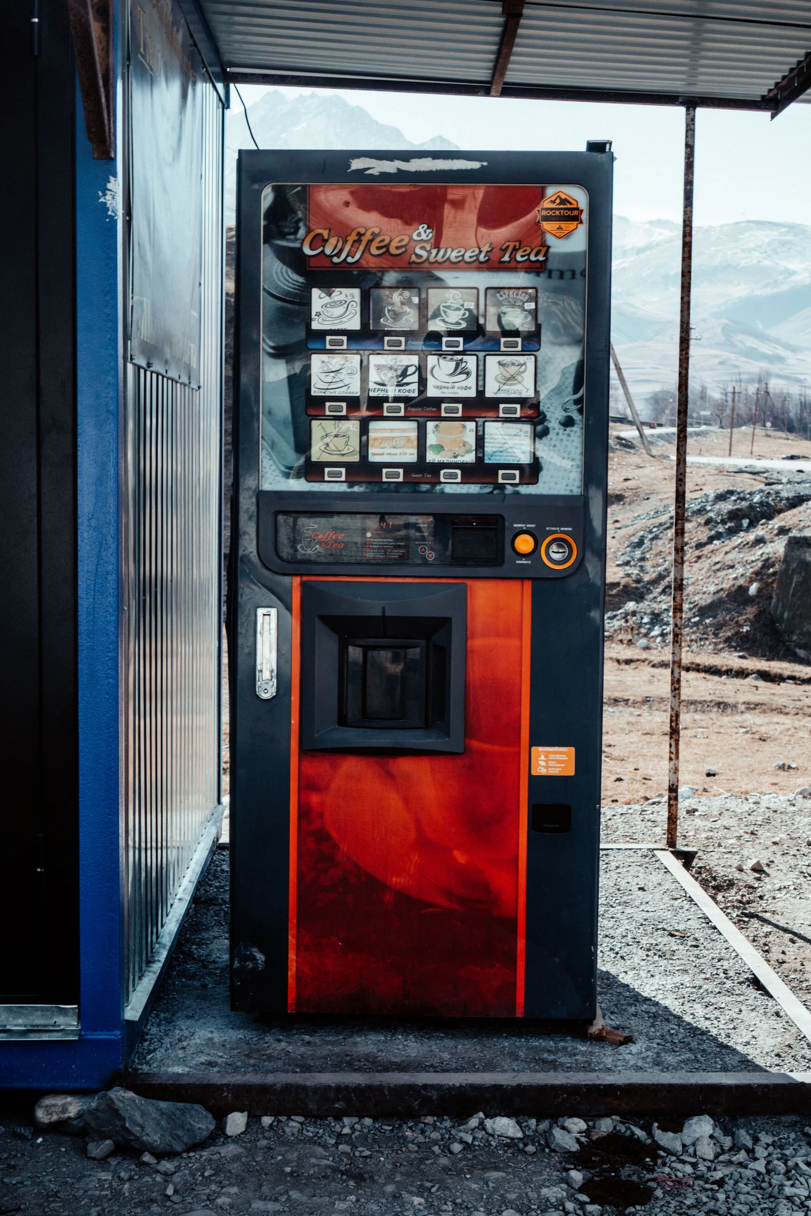Un distributeur automatique de boissons chaudes portant l'inscription Coffee and Sweet Tea, installé en extérieur devant un paysage de montagnes