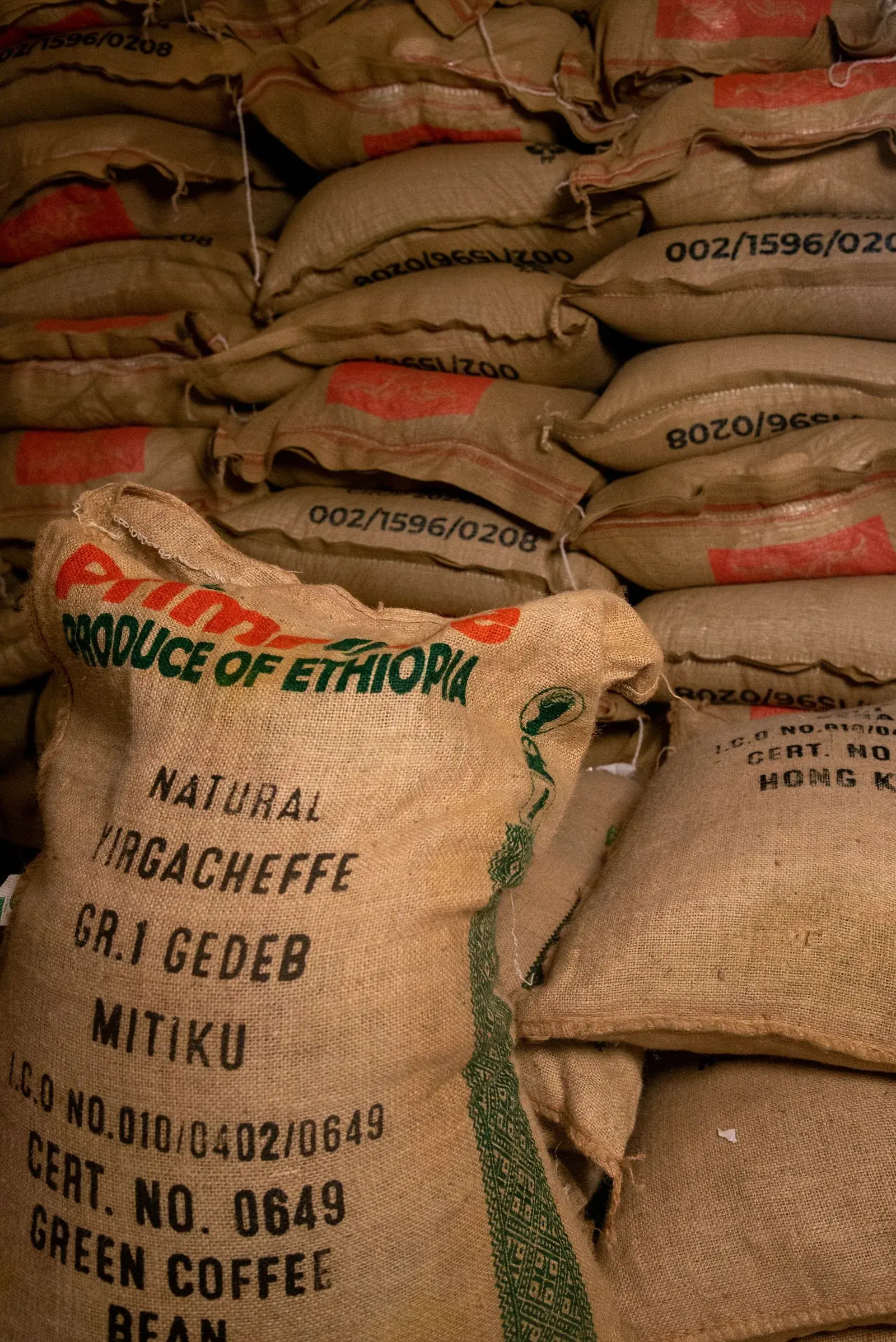 Sacs de jute empilés, celui du premier plan marqué « Produce of Ethiopia, natural Yirgacheffe Gr.1 Gedeb », avec numéros de lot et de certificat.