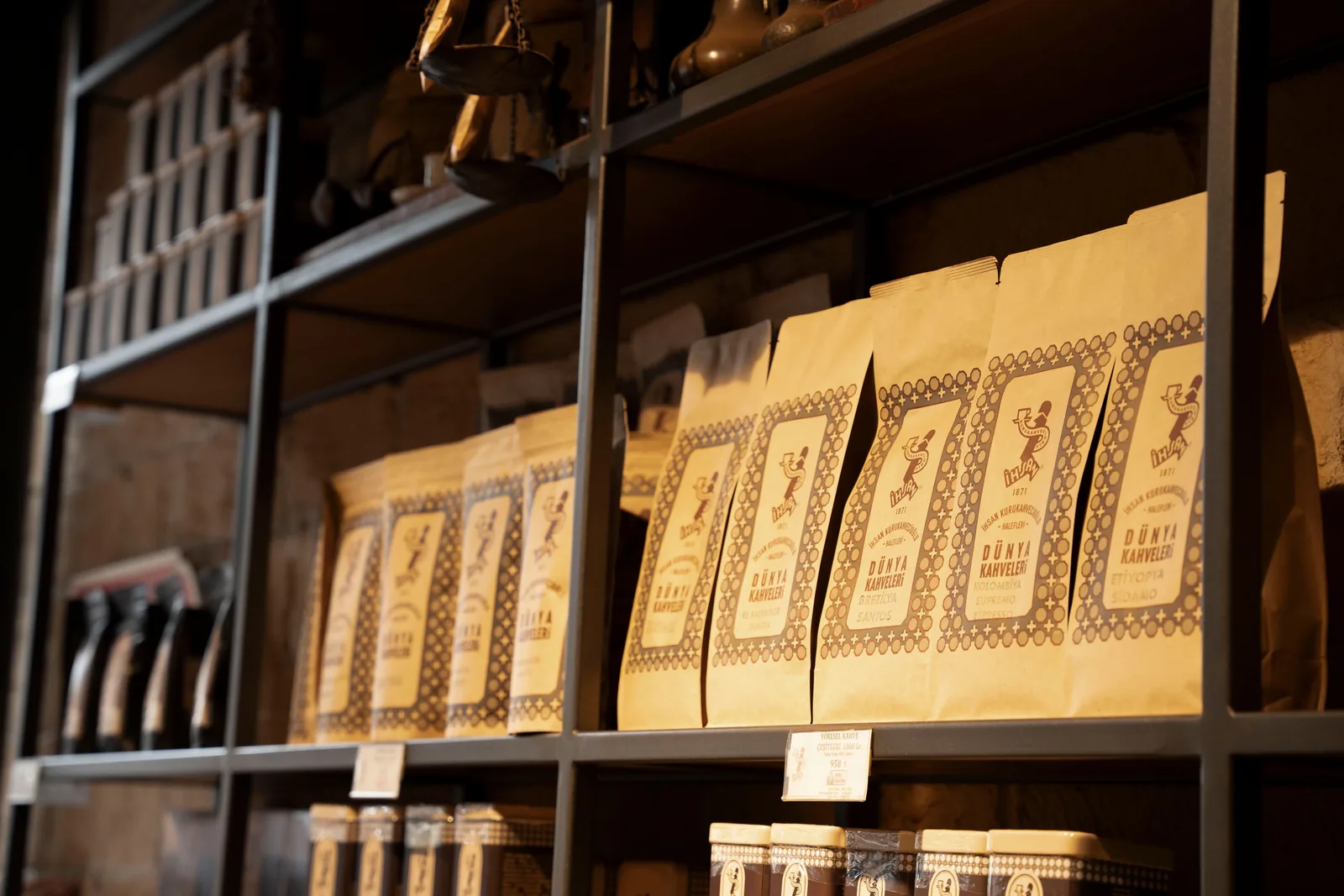 Des sachets de café artisanal portant chacun un pays d'origine sont alignés sur une étagère en bois, avec une étiquette de prix visible au premier plan