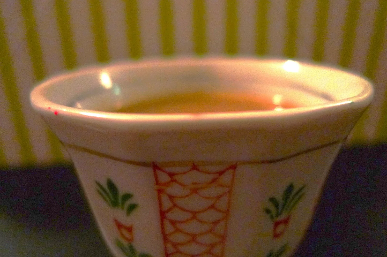 Photographie rapprochée d'un finjan, petite tasse sans anse remplie de café arabe clair, tenue au-dessus d'une soucoupe.