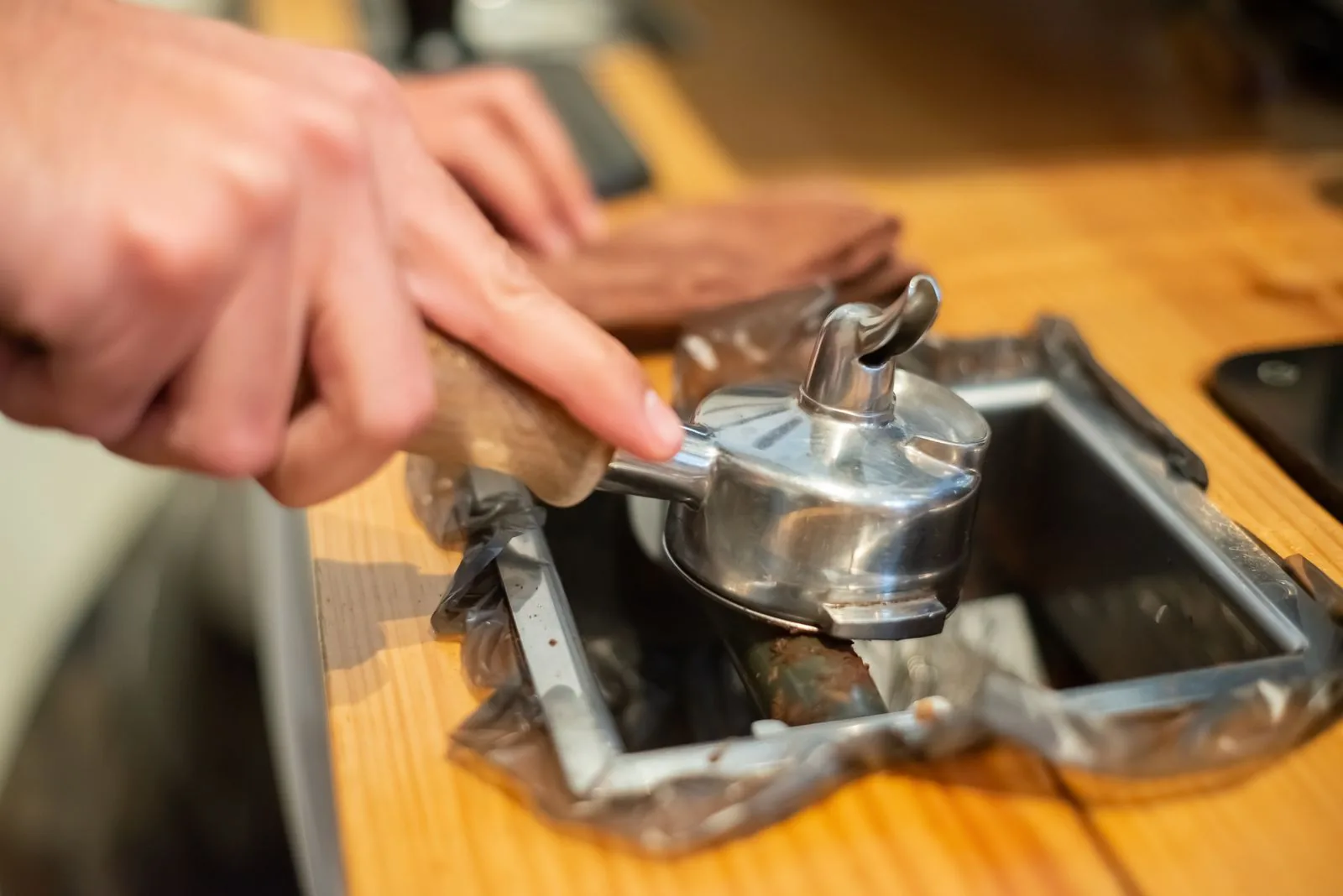 Mains retournant un porte-filtre au-dessus d'un bac de métal, la galette de café usé en train de se détacher sur le rebord.