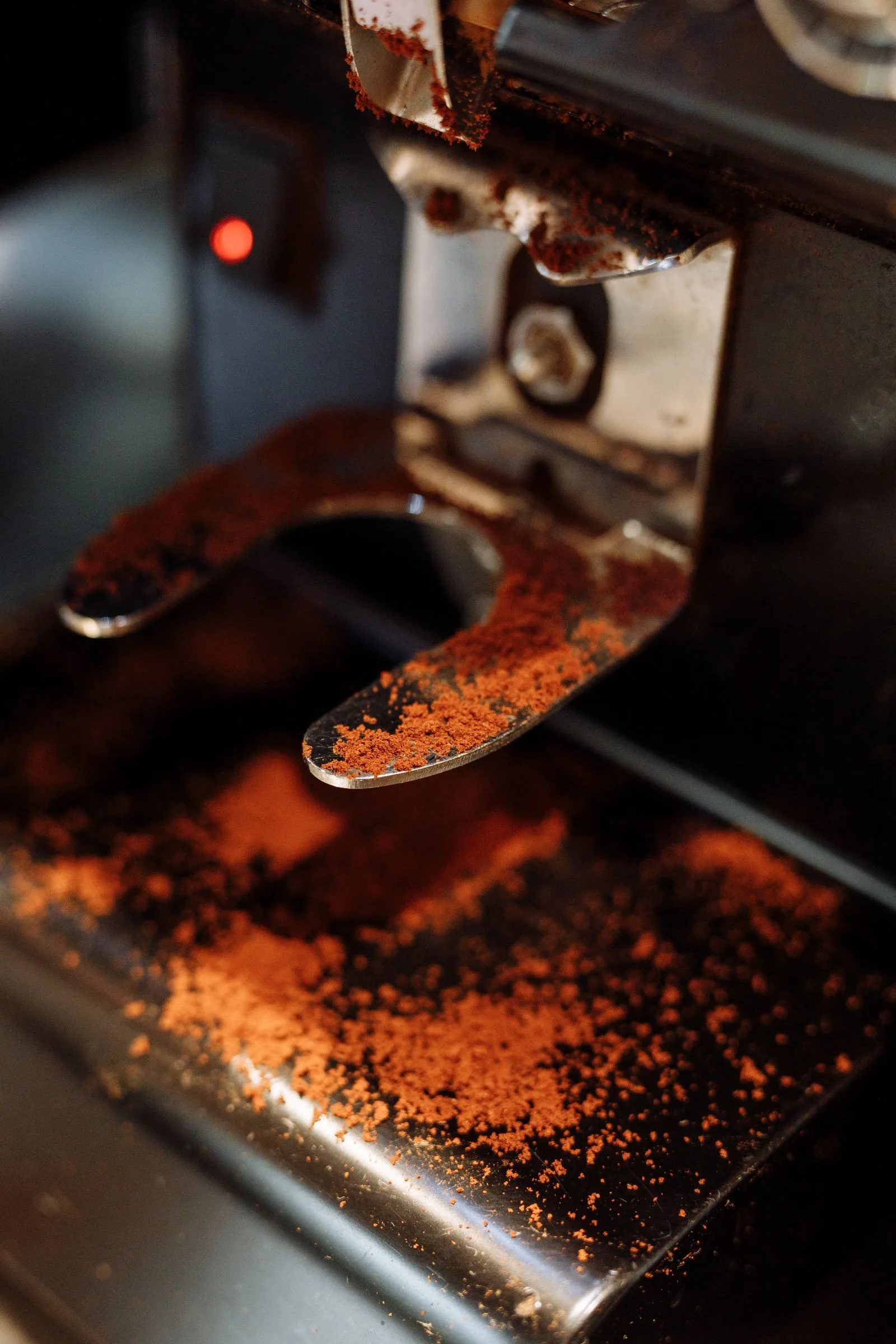 Détail d'une machine à espresso dont le porte-filtre, la grille et le plan d'inox sont recouverts de marc de café renversé.