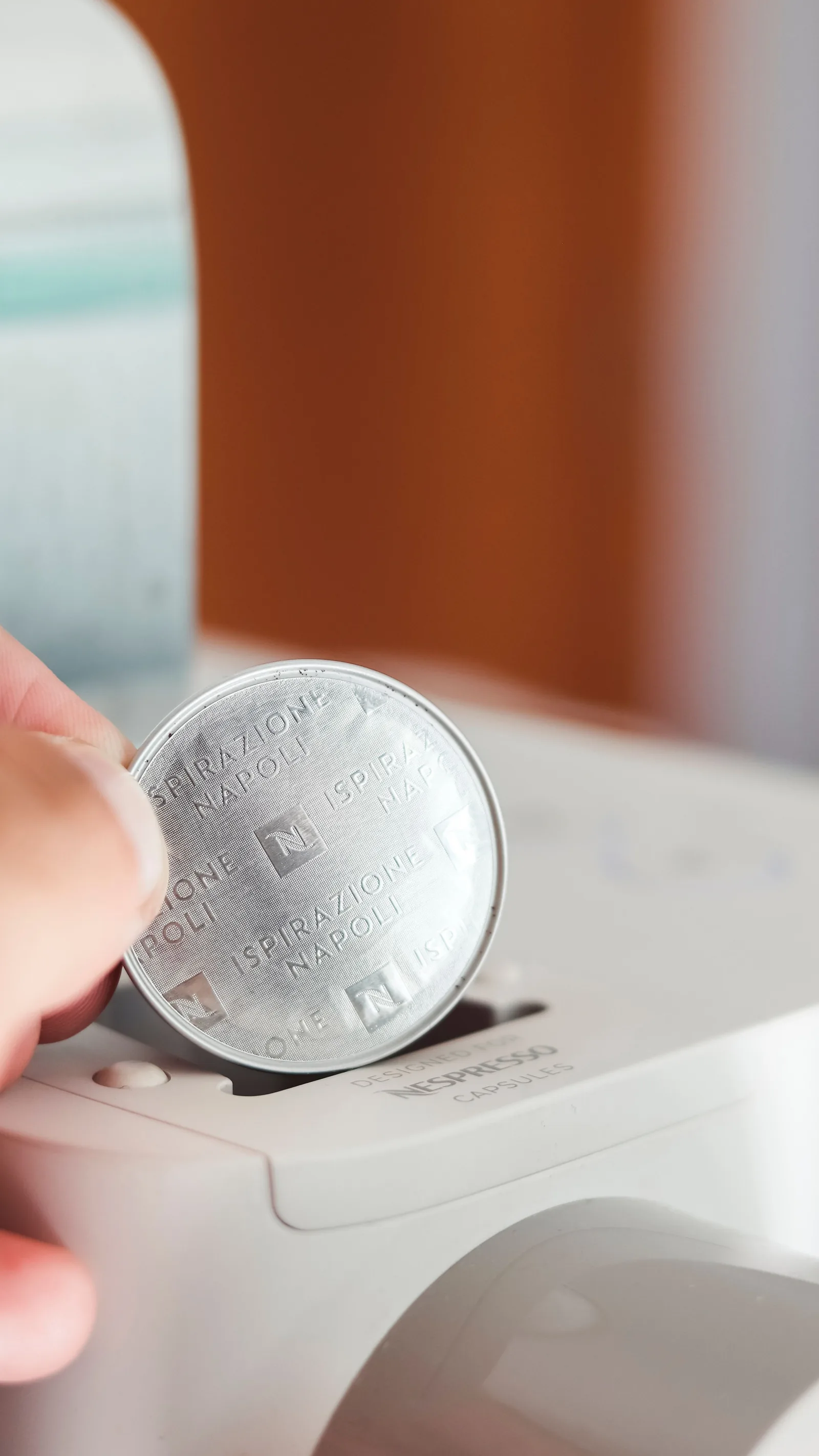 Une main insère une capsule de café argentée dans le réceptacle d'une machine à dosettes blanche