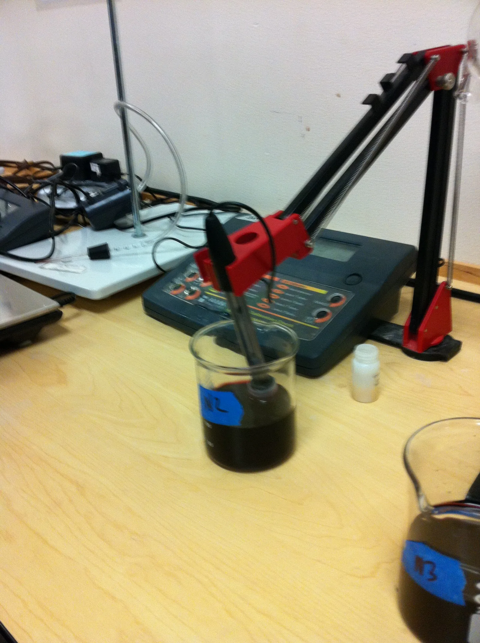 La sonde d'un pH-mètre de paillasse plonge dans un bécher contenant un échantillon liquide sombre ; l'image montre un test sur du vin, mais le même type d'appareil sert à contrôler le pH d'une fermentation de café
