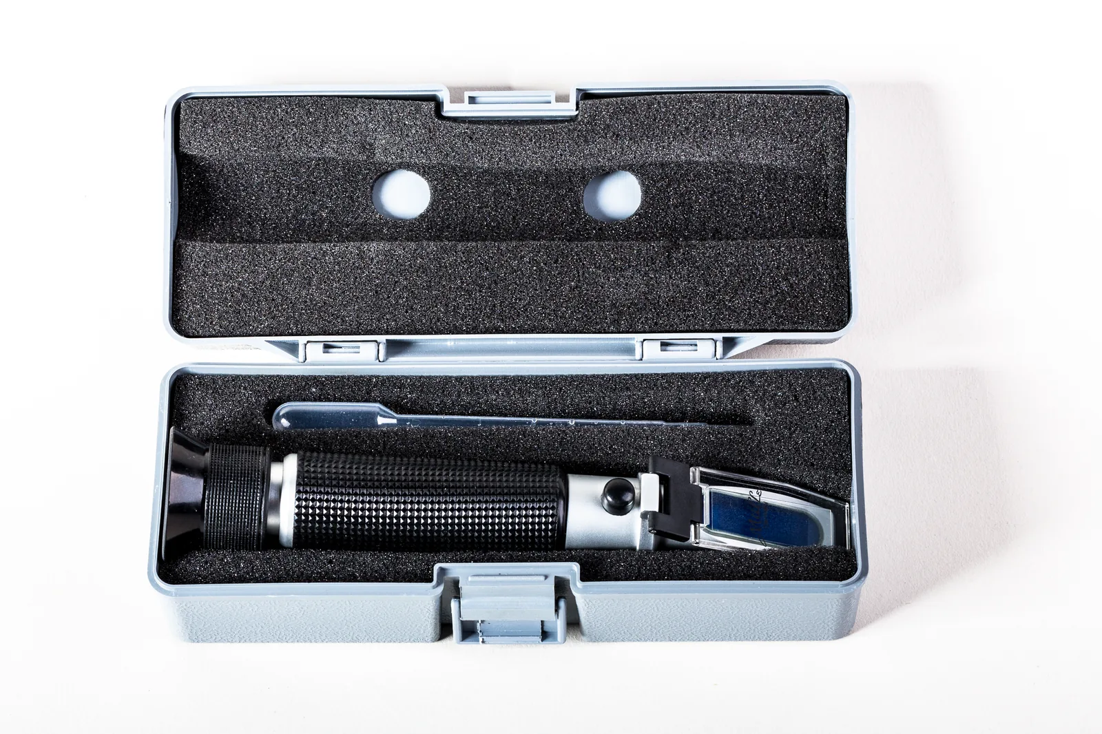 Un réfractomètre optique à main, rangé ouvert dans son étui avec sa pipette compte-gouttes