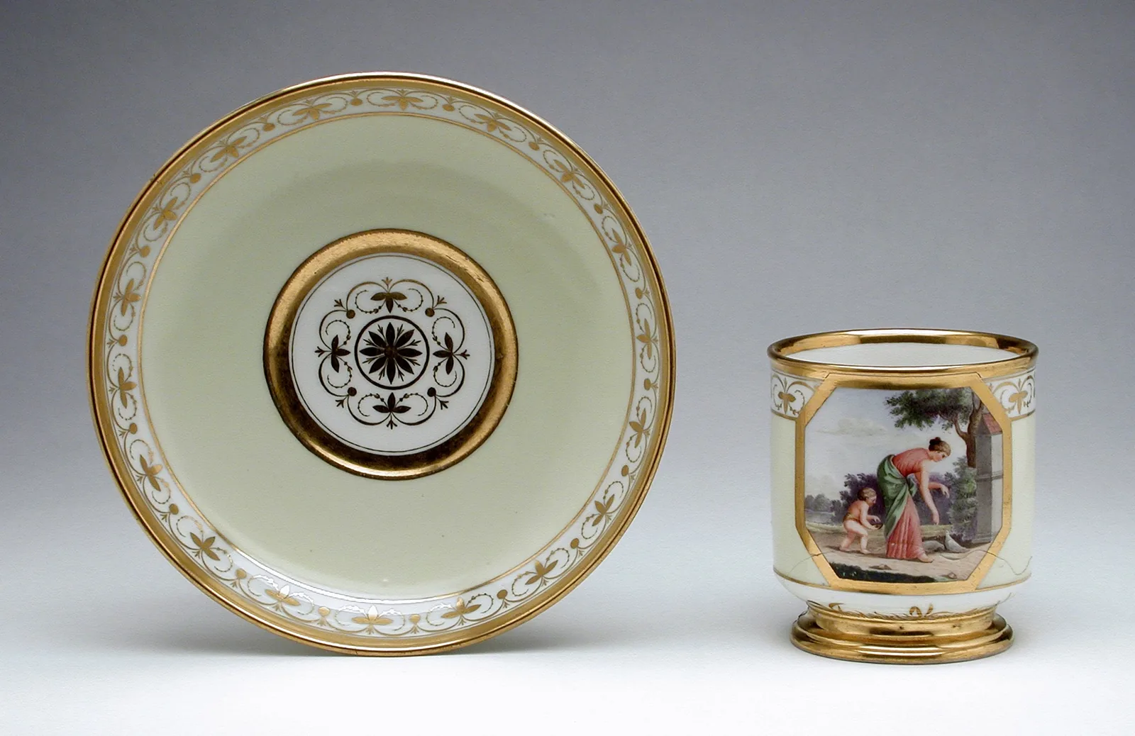 Photographie d'un gobelet à café de porcelaine et de sa soucoupe, fond crème et filets d'or, le gobelet portant un médaillon peint d'une scène de personnages à l'antique et la soucoupe une rosace centrale.