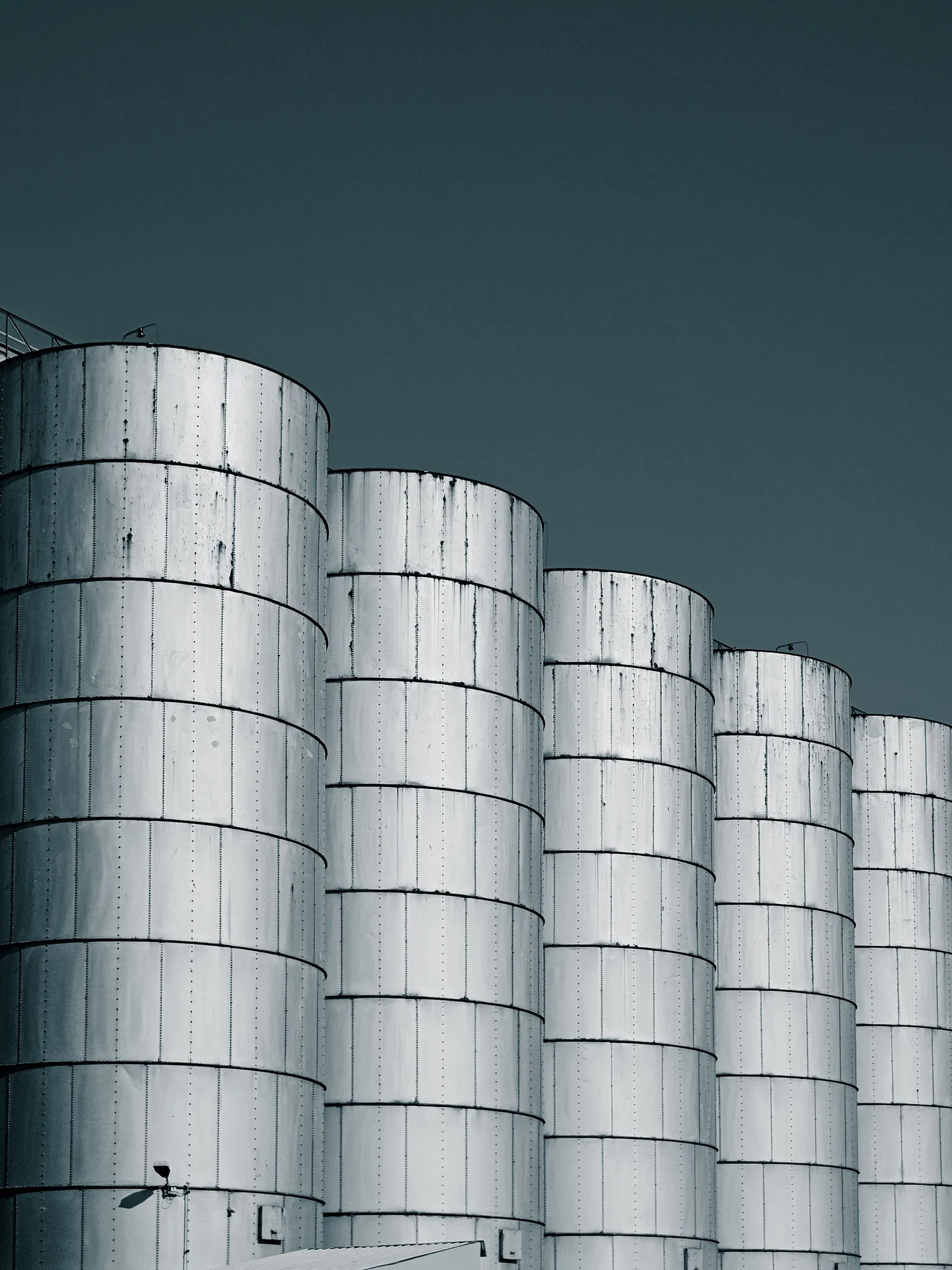 Une rangée de silos cylindriques en métal argenté se découpant sur un ciel bleu foncé, vus en contre-plongée