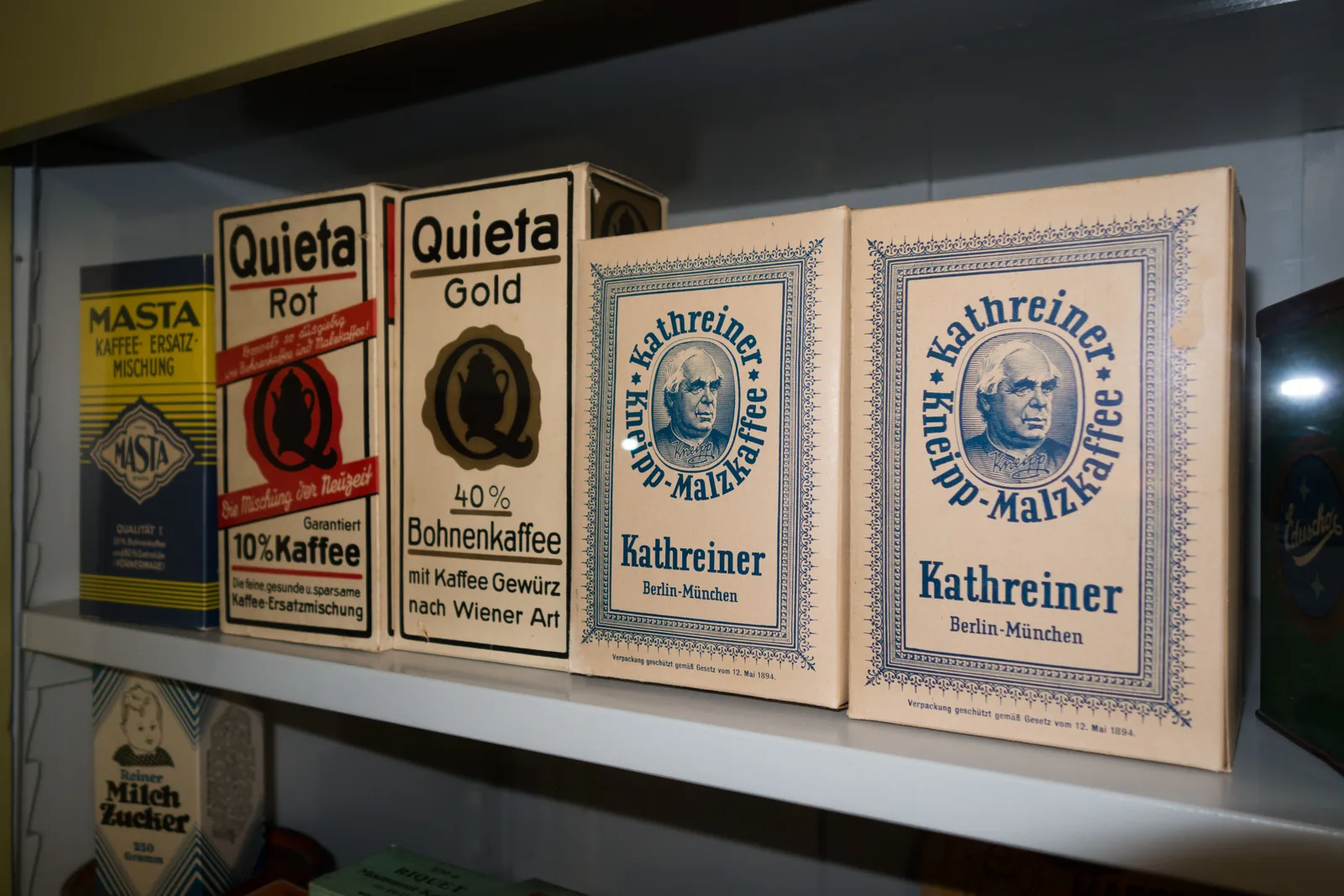 Photographie de trois paquets anciens de succédanés de café, Masta, Quieta et Kathreiner, alignés avec leurs étiquettes imprimées et leurs mentions de marque.