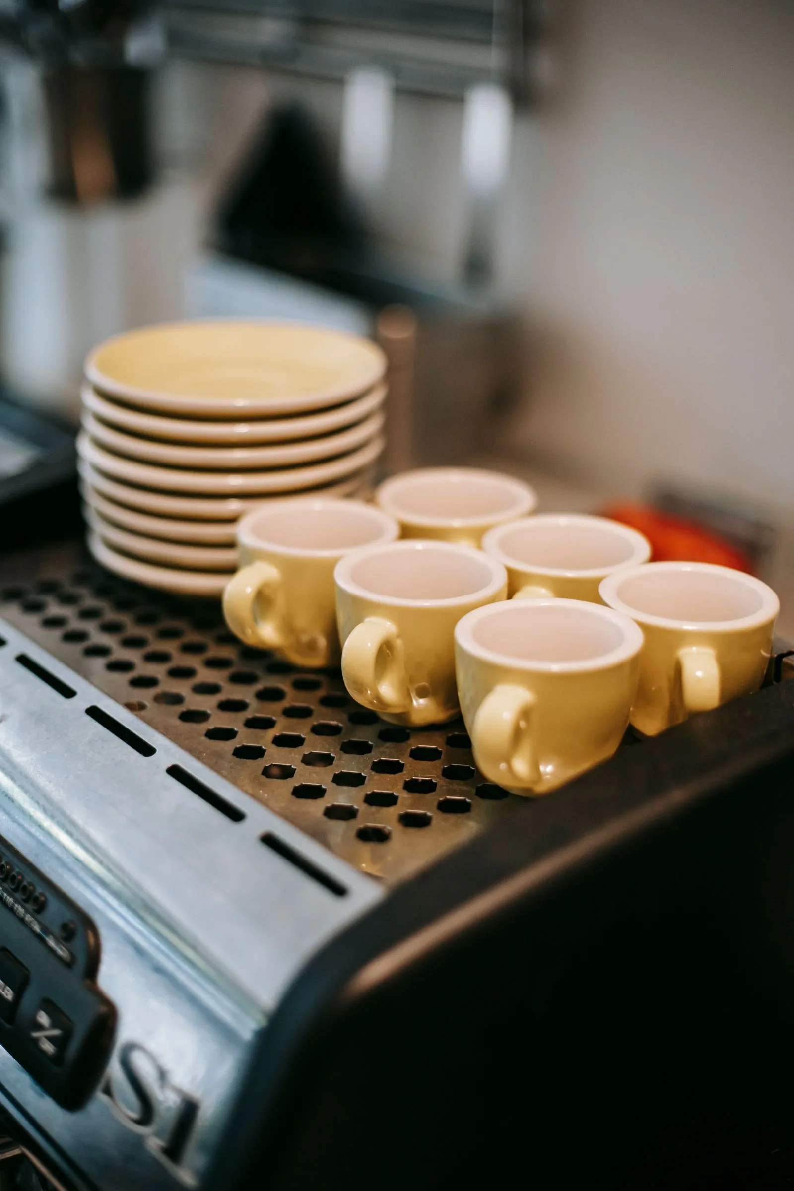 Pile de soucoupes et six tasses jaunes retournées sur la grille supérieure d'une machine à espresso.