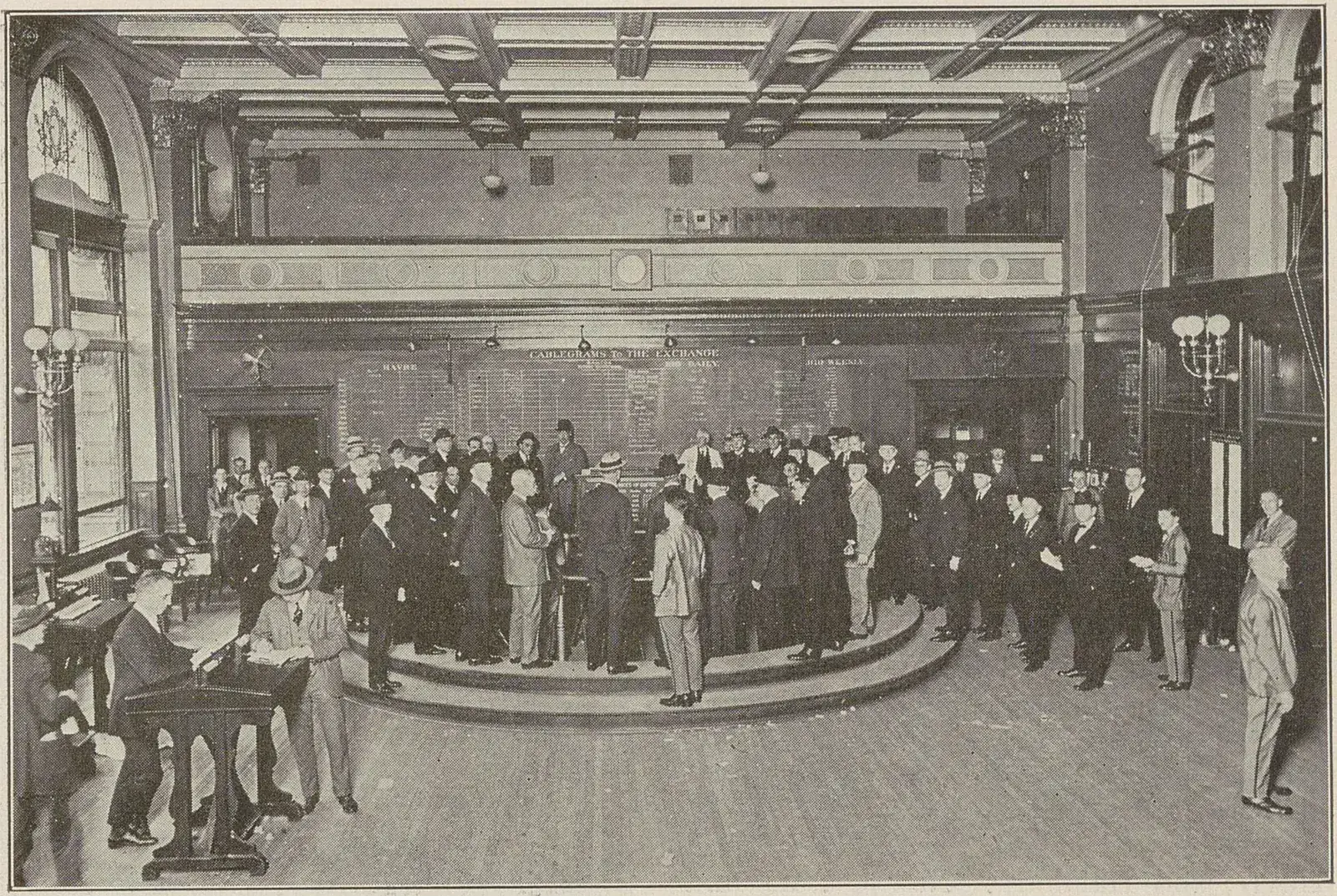 Salle de marché où une centaine d'hommes en costume se pressent autour de la corbeille de cotation circulaire.
