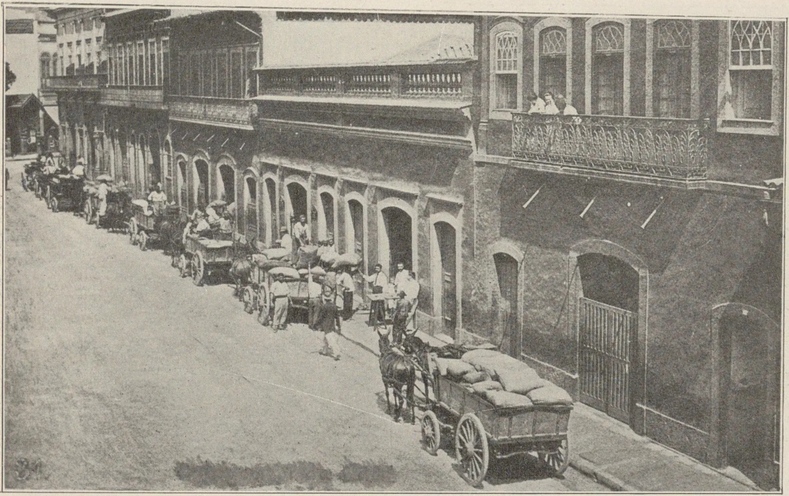 Rue étroite bordée d'entrepôts à arcades, encombrée de charrettes chargées de sacs de café.