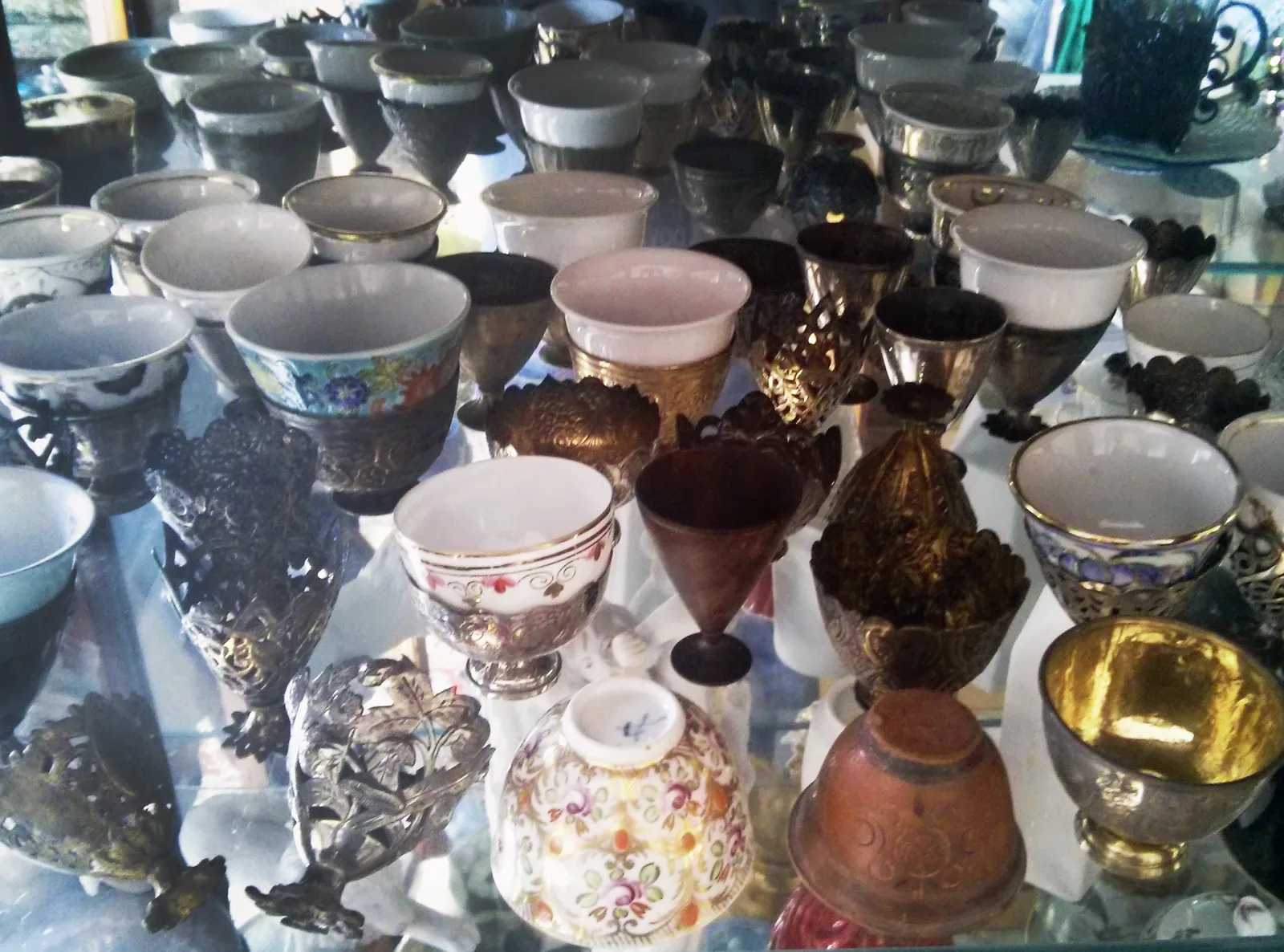 Photographie d'un ensemble de zarfs ottomans, ces porte-tasses sans anse en argent, en tombak doré, en bois et en cuivre, présentés avec les petites tasses de porcelaine qu'ils recevaient.
